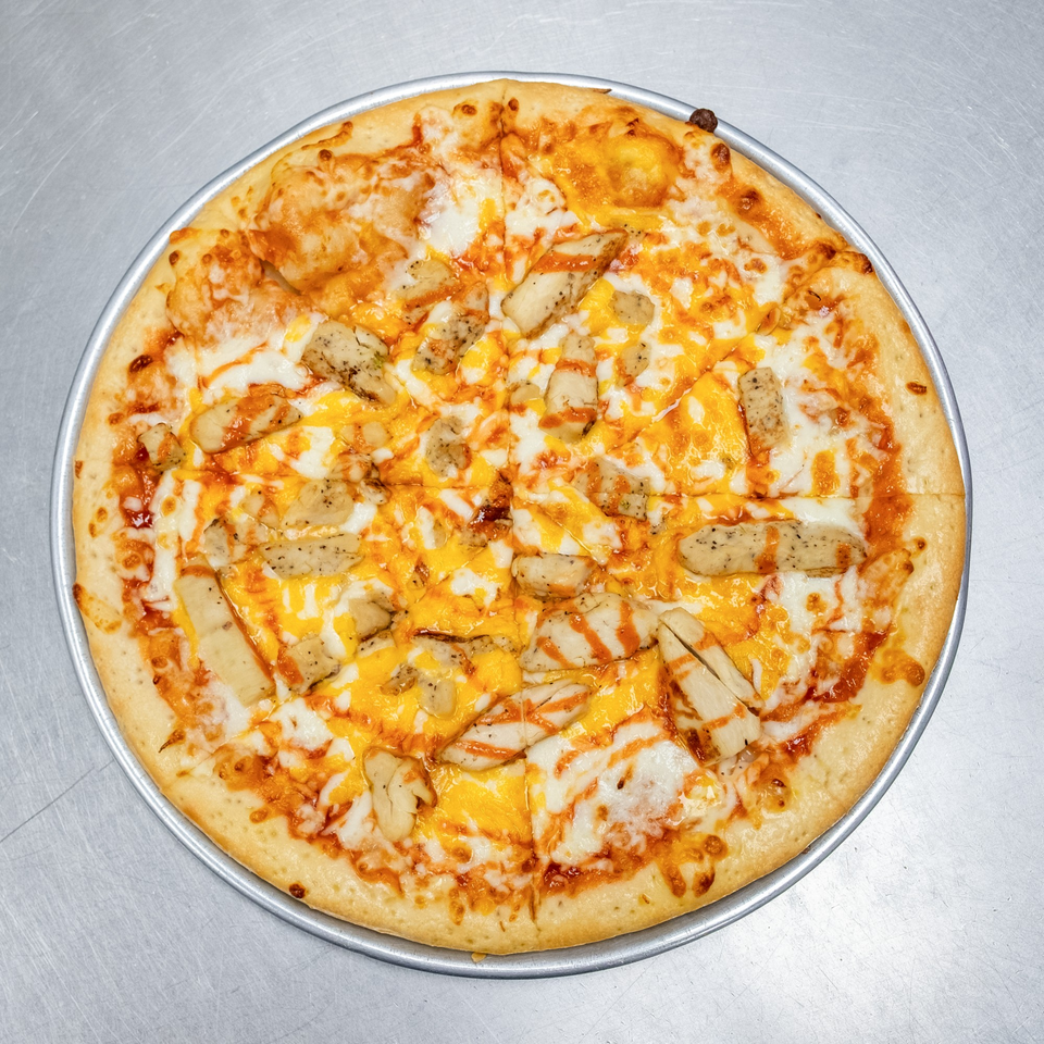 A whole buffalo chicken pizza, topped with white and orange cheese, and chicken pieces.