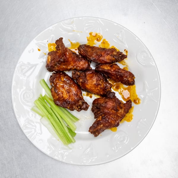 Six glazed chicken wings with celery sticks on a white plate.