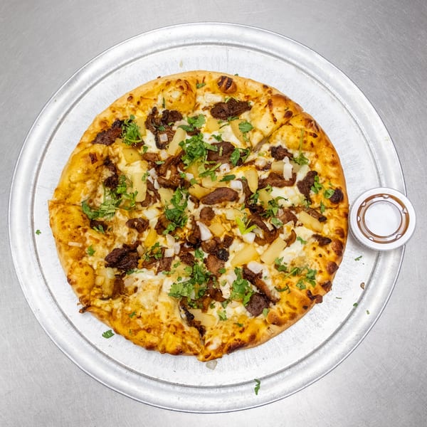 A whole pizza with beef, pineapple, onions, and cilantro on a metal tray.