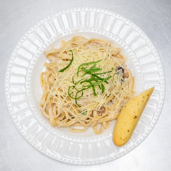 Creamy pasta with mushrooms, topped with shredded cheese and basil, served with a breadstick.