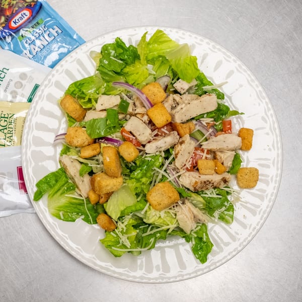 Chicken Caesar salad with croutons, red onion, and shredded cheese on a white plate.