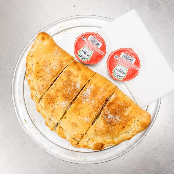 A sliced calzone with two marinara sauce cups on a metal pizza tray.