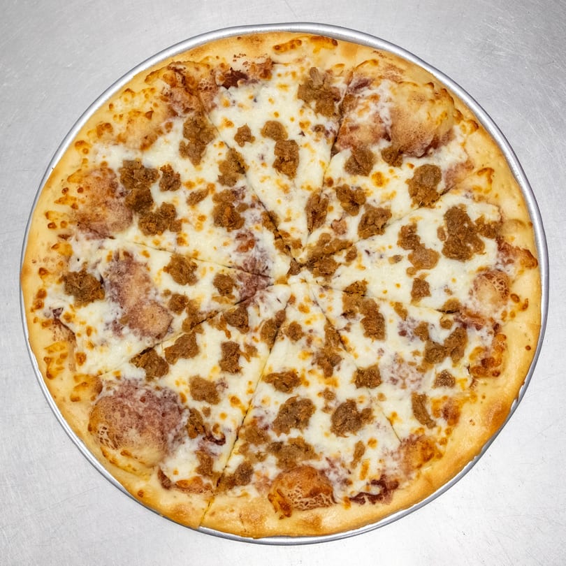 A whole, sliced pizza with white cheese and crumbled sausage on a metal tray.