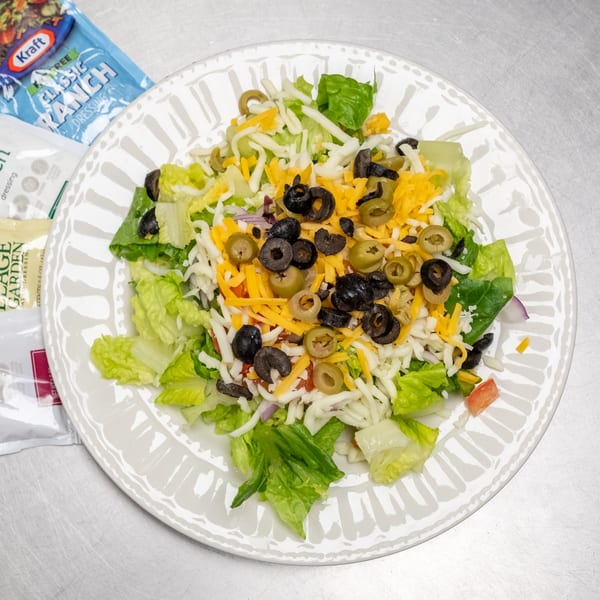 A fresh salad with lettuce, shredded cheese, black olives, and green olives on a white plate.