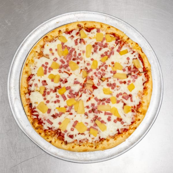 A whole Hawaiian pizza with pineapple and ham on a metal tray.