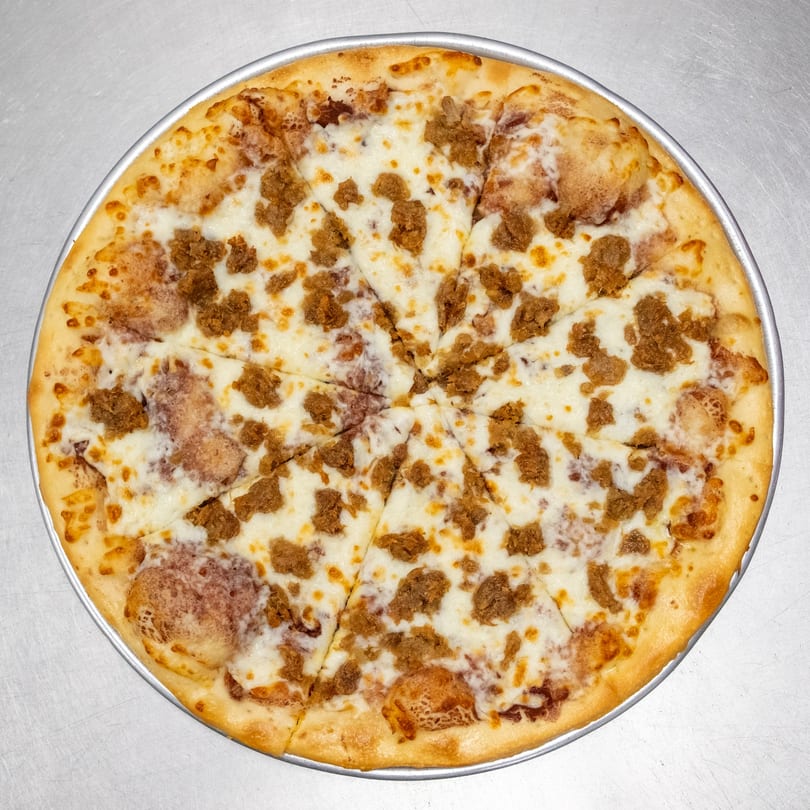 A whole round pizza with white cheese and crumbled sausage, sliced into eight pieces.